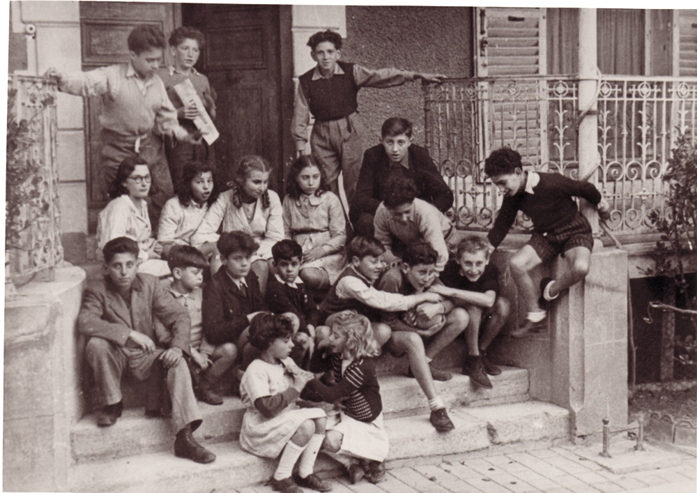 Children sitting and goofing around on steps outside the entrance to a house.
