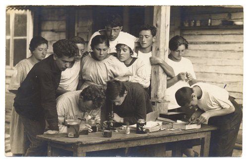 <p>A group of students examines a specimen under a microscope at a summer camp. Puszkarnia, Poland (now Lithuania), 1922.<br /></p>
<p><em>Photograph by D. G. Aliber. From the Archives of the YIVO Institute for Jewish Research, New York.</em><br /></p>