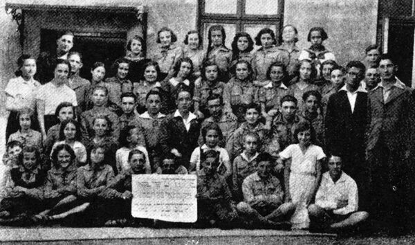 Une cinquantaine d’élèves posent dehors pour la photo de classe. À l’avant, des élèves tiennent une affiche en yiddish.