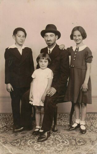 A man in a hat sits in a chair with three children standing around him.