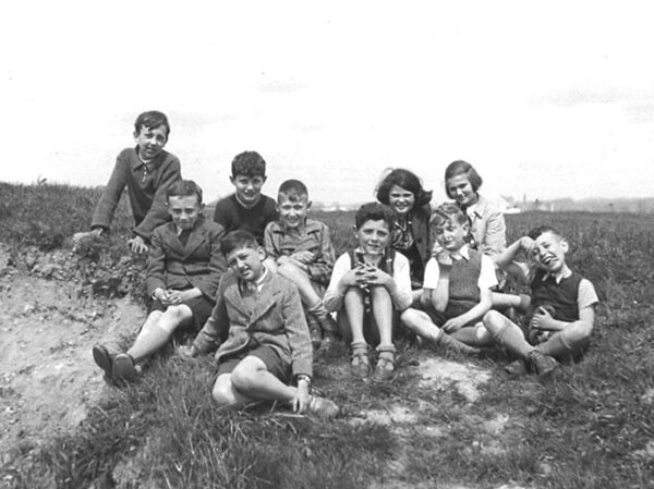 A group of children sitting on the ground outside, smiling and making faces for the camera.