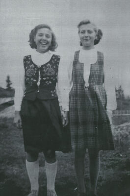 Two girls standing next to each other outdoors, laughing and smiling at the camera.