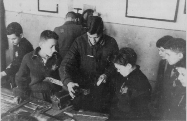 Young boys with Stars of David on their clothing standing around a teenage boy, looking on as he demonstrates use of a machine.