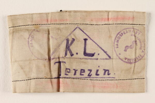 Morceau d’étoffe pâle, tachée, sur laquelle on a inscrit un triangle, des tampons et « K. L. Terezin ».