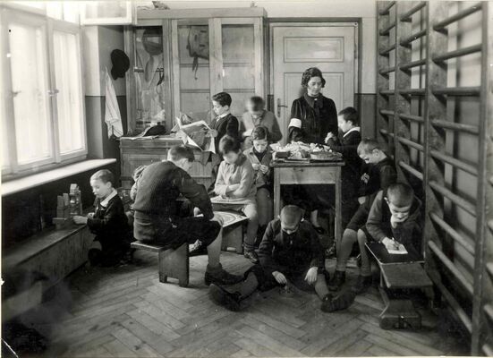 Children and a teacher in various poses, playing, reading and writing in a small room, words in Polish printed under the picture.