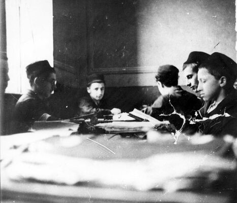 Boys sitting around a table with books and papers on it, reading.