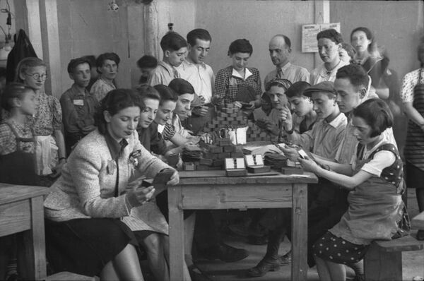 Young people sitting and standing around a table, examining items on the table.
