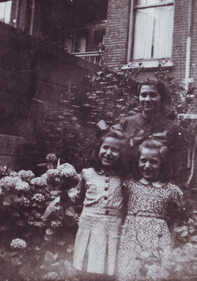 Coiffées de boucles, deux fillettes souriantes posent avec une femme dans un jardin en fleurs. Coiffées de boucles, deux fillettes souriantes posent avec une femme dans un jardin en fleurs.