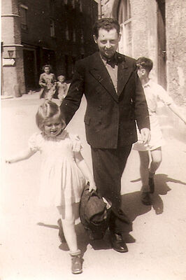 Young girl holding a bag walking down a street with a man who has his arm protectively on her back.