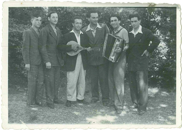 Six young men standing in a row outdoors, posing with musical instruments.