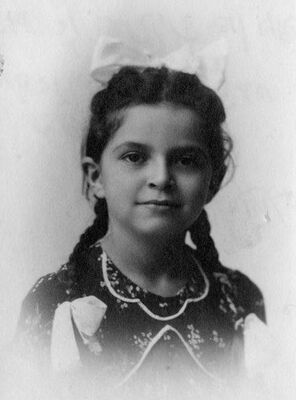 Close up of girl with her hair done in braids and bows, smiling slightly at the camera.