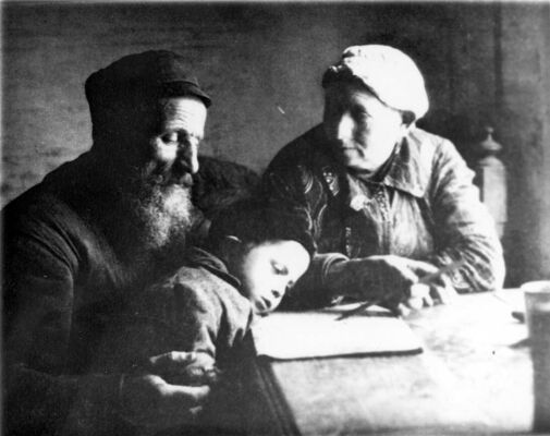 A bearded man, a woman and a young child sitting and studying a page as the child slumps over a table.