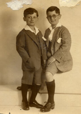 Two children in formal clothing, close in age posing next to each other against a light background, smiling slightly.