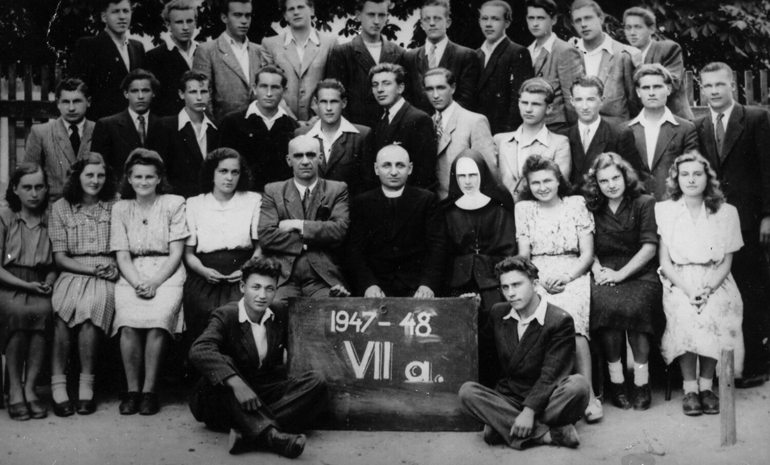 Class picture of teenagers in formal clothing with teachers and a nun sitting front and centre.