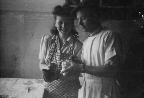 Young woman holding tools and smiling at the camera, standing close to young man holding and looking at dental mold.