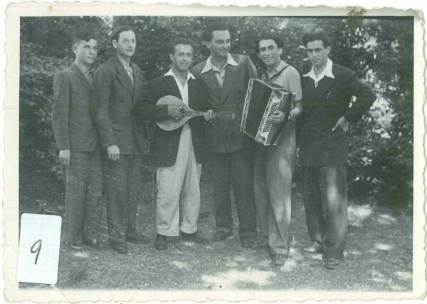 Six jeunes hommes, dont deux munis d’instruments de musique, posent en une rangée.