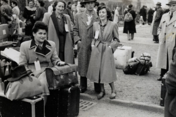 Une femme est assise sur une valise. Près d’elle, des personnes attendent.