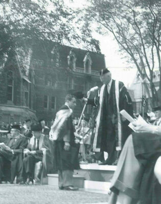 Un jeune homme portant une toge reçoit son mortier de la main d’un homme sur un podium.