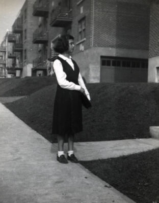 Une jeune fille se tient cartable à la main devant une rangée d’immeubles identiques.