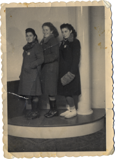 Three young women posing on a small, raised platform, wearing winter coats with Stars of David on them.