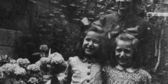 A woman and two young girls standing in a garden smiling at the camera.