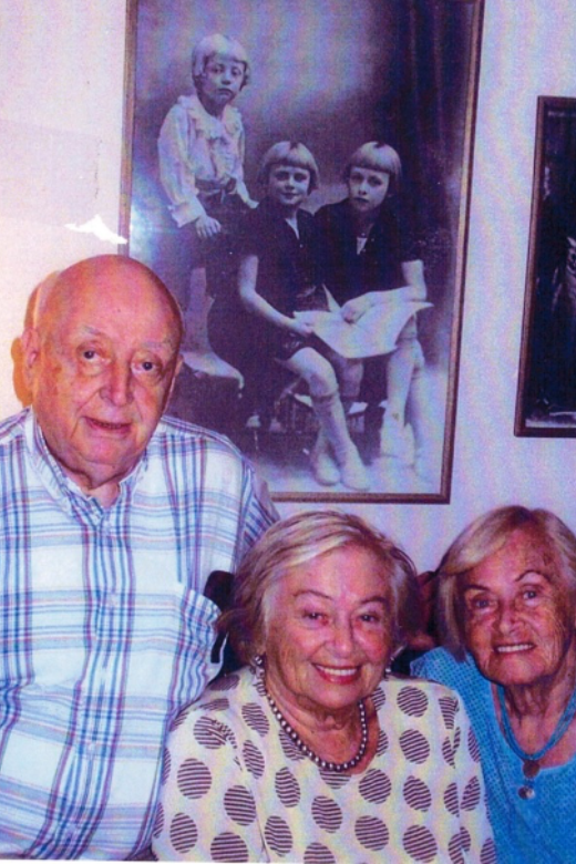 Freda (centre), with her brother, Harry (Mietek), and sister, Miriam, in front of their childhood picture of them in the same order. Toronto, circa 2014. The childhood photo was taken in Lodz, Poland, before the war.